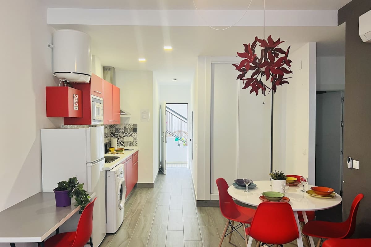 A modern kitchen with red cabinets, a white refrigerator, and a dining area with red chairs and a white table.