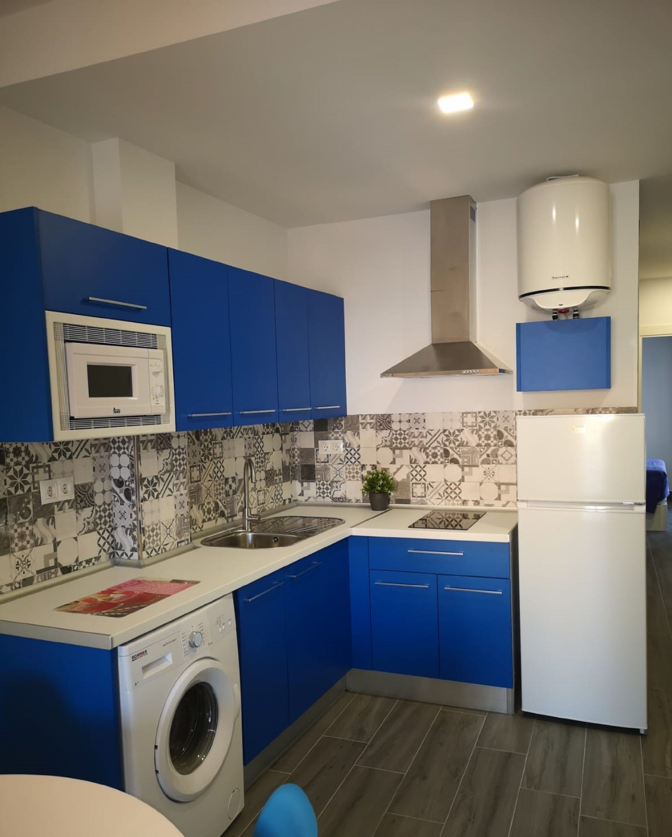 Une cuisine moderne avec des meubles bleus, un four à micro-ondes encastré, un lave-linge et un réfrigérateur.
