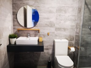 A modern bathroom with a rectangular sink, a round mirror, a toilet, and a shower area. - Bnbook Medea Apartments (Fuengirola)