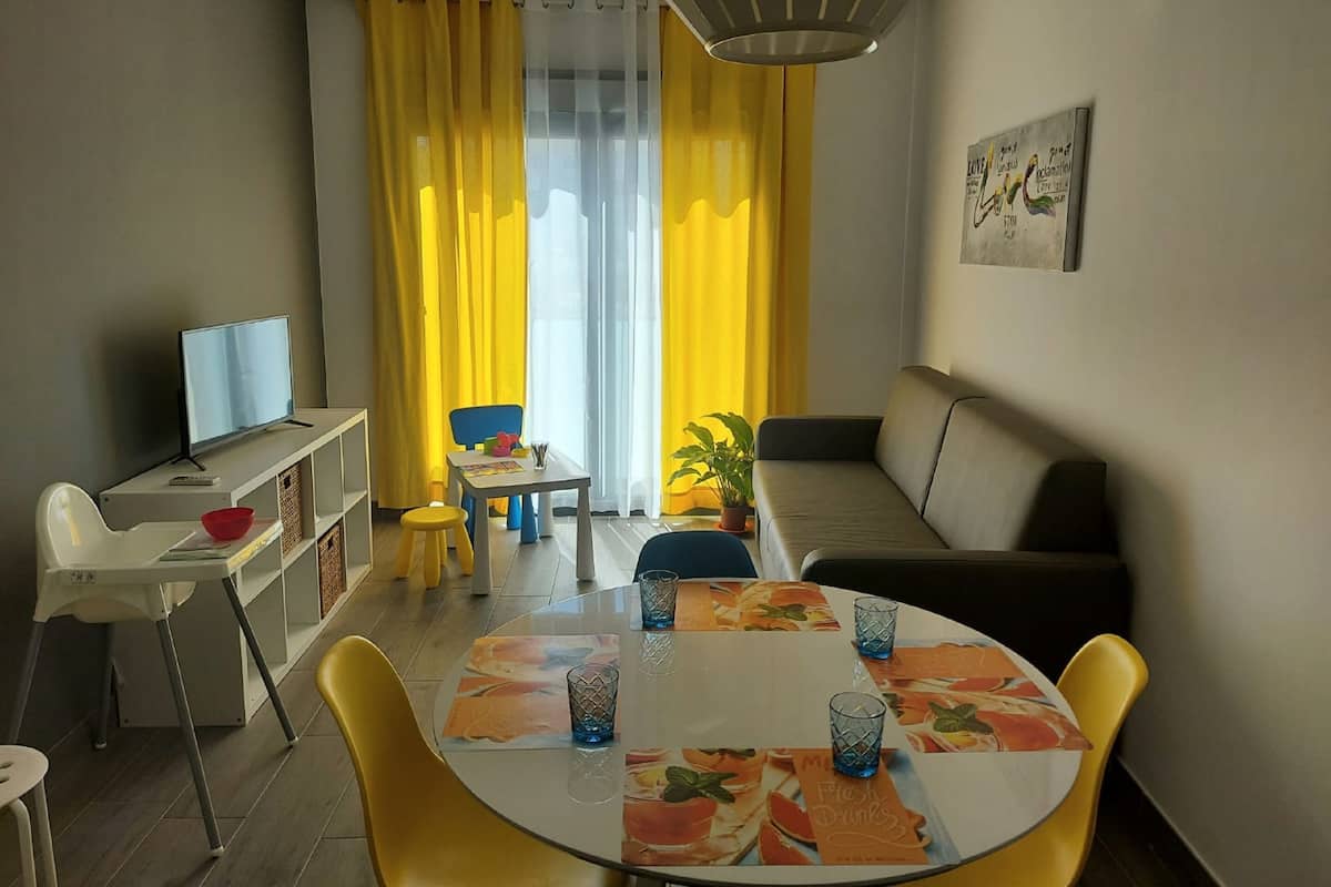 A modern living room with a sofa, a dining table with chairs, a TV, and a bookshelf.