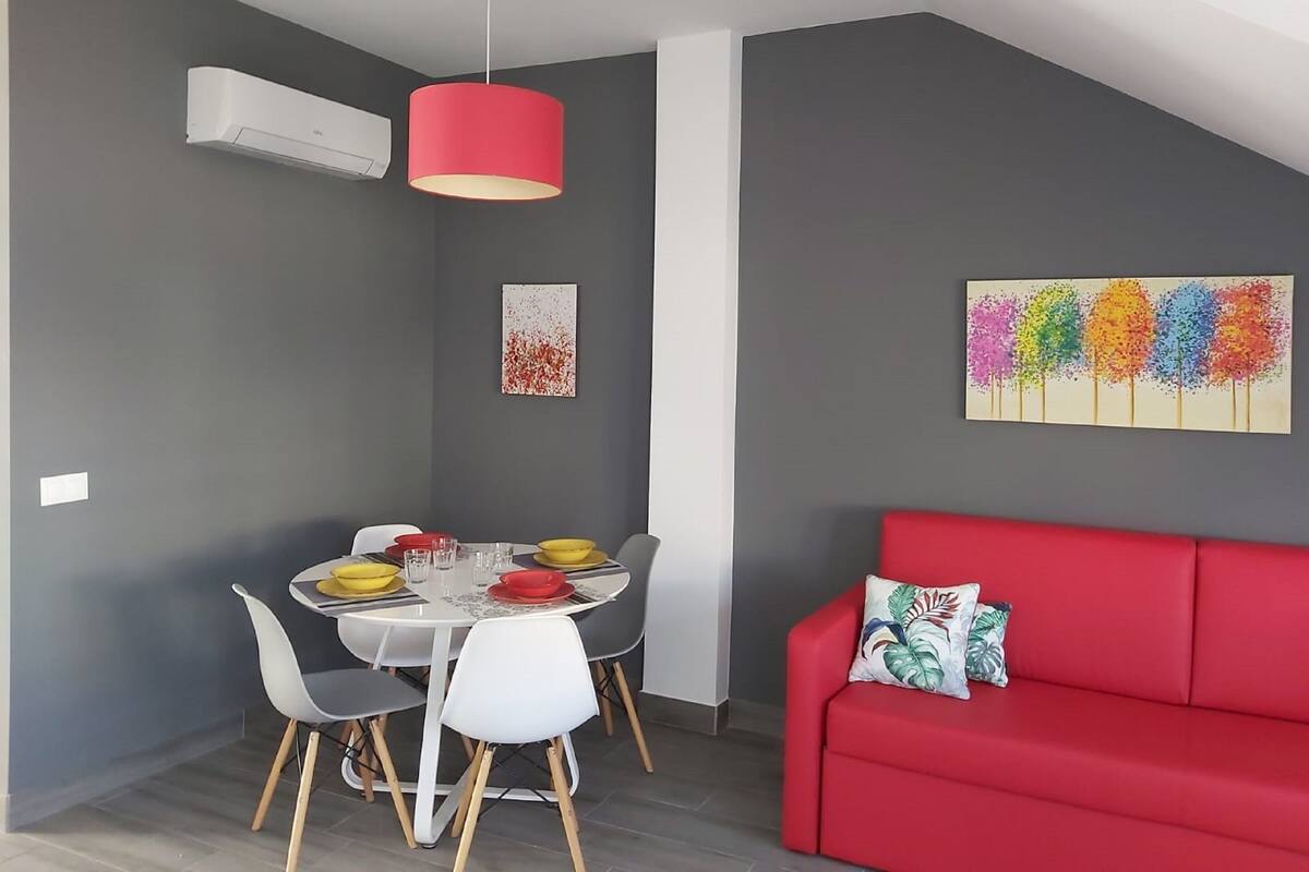 A modern living space with a dining area, a red sofa, and artwork on the walls.
