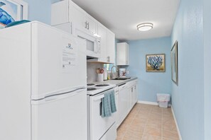 Compact kitchen with refrigerator, microwave, and stove, featuring a tiled floor and framed artwork.