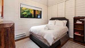 A bedroom with a large bed, a window with a view of trees, a wooden headboard, and a chandelier.