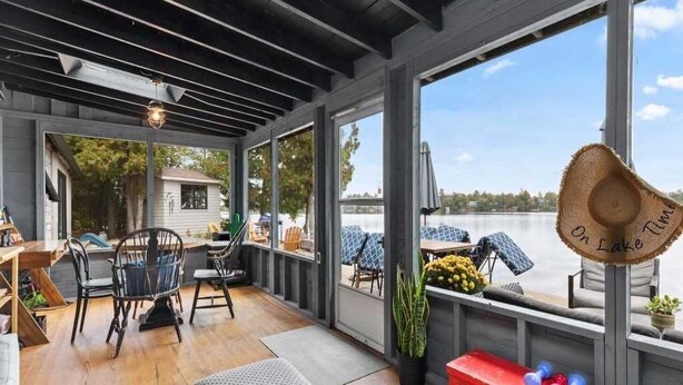 A covered outdoor area with a wooden floor, seating, and large windows overlooking a body of water.