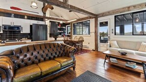 A spacious living area with a leather sofa, wooden flooring, and a large window offering a view.