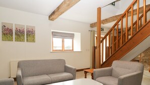 Een woonkamer met een grijze bank, een witte salontafel en een houten trap.