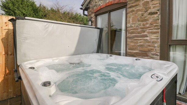 Een jacuzzi met bedieningspaneel, voor een stenen gebouw met een houten omheining en een raam.