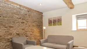 Een kamer met een stenen muur, twee grijze fauteuils, een witte salontafel en een vloerlamp.