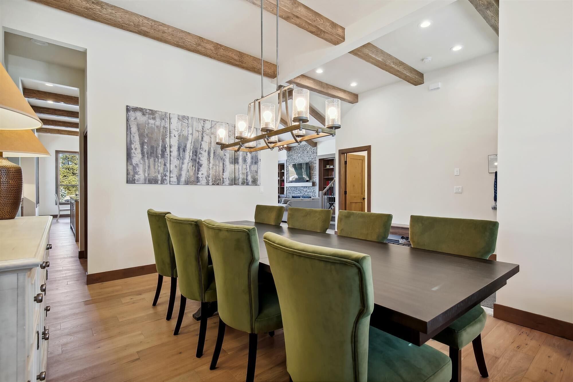 Een eetgedeelte met een lange tafel en groene bekleden stoelen, een houten plafond en een moderne kroonluchter.