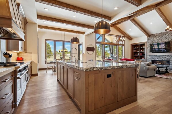 A spacious kitchen with a large island, wooden cabinets, and a stone fireplace.