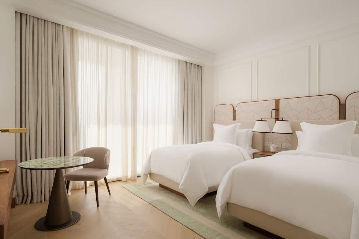 Une chambre d’hôtel avec deux lits, une table ronde, une chaise et une table de chevet avec des lampes.