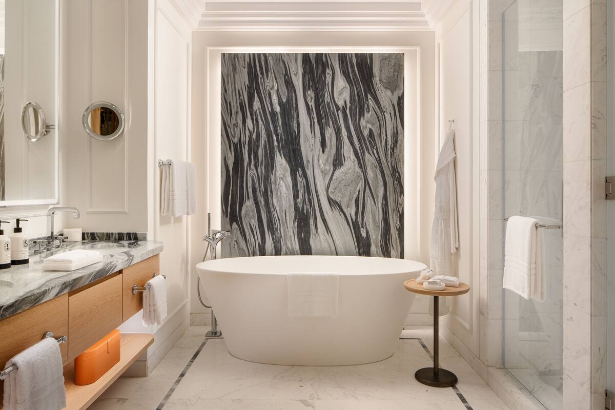 Une salle de bain moderne avec une baignoire sur pieds, un mur en marbre et une douche à parois de verre.