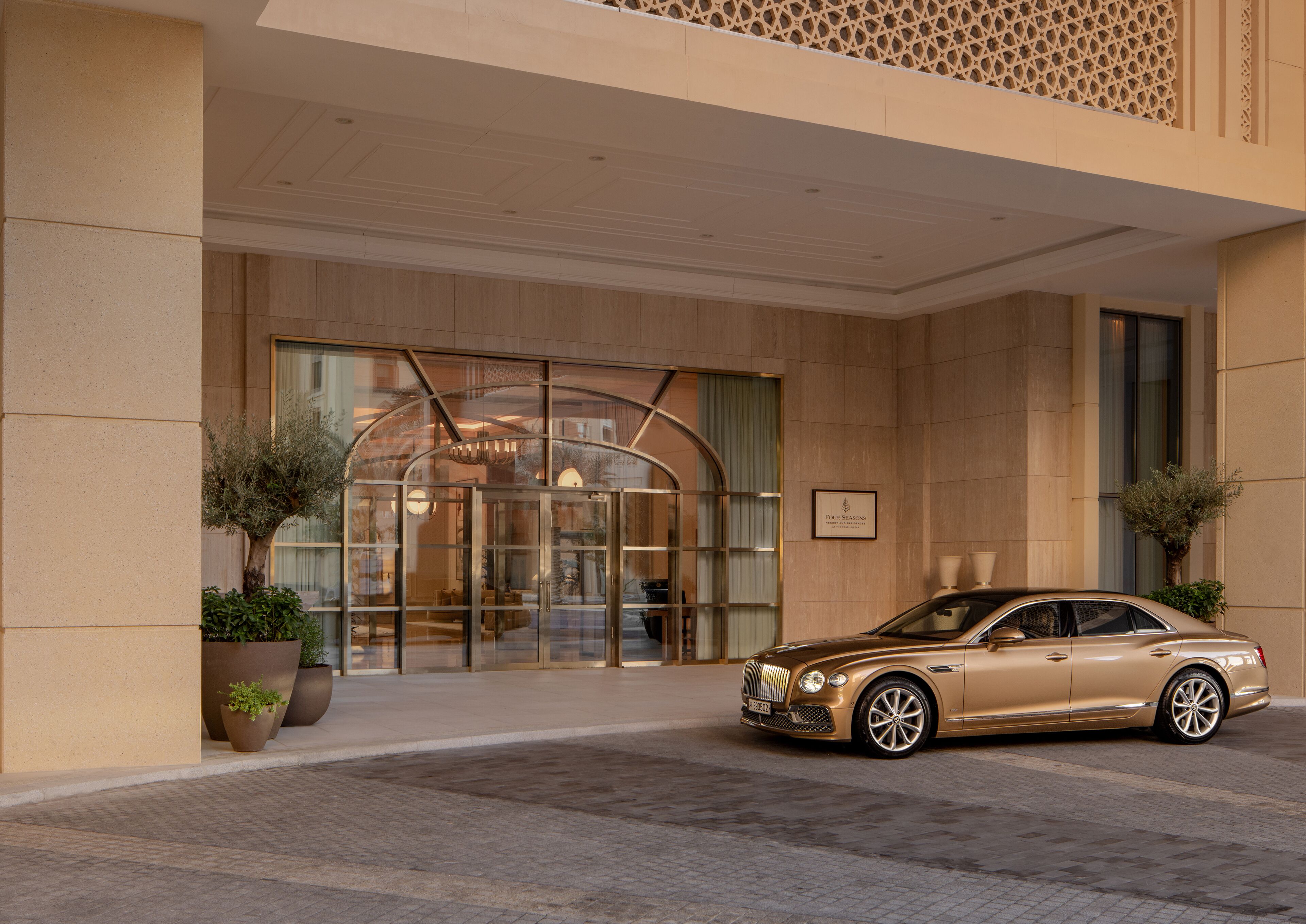 A luxury hotel entrance with a glass door, a car parked in front, and potted plants on either side.