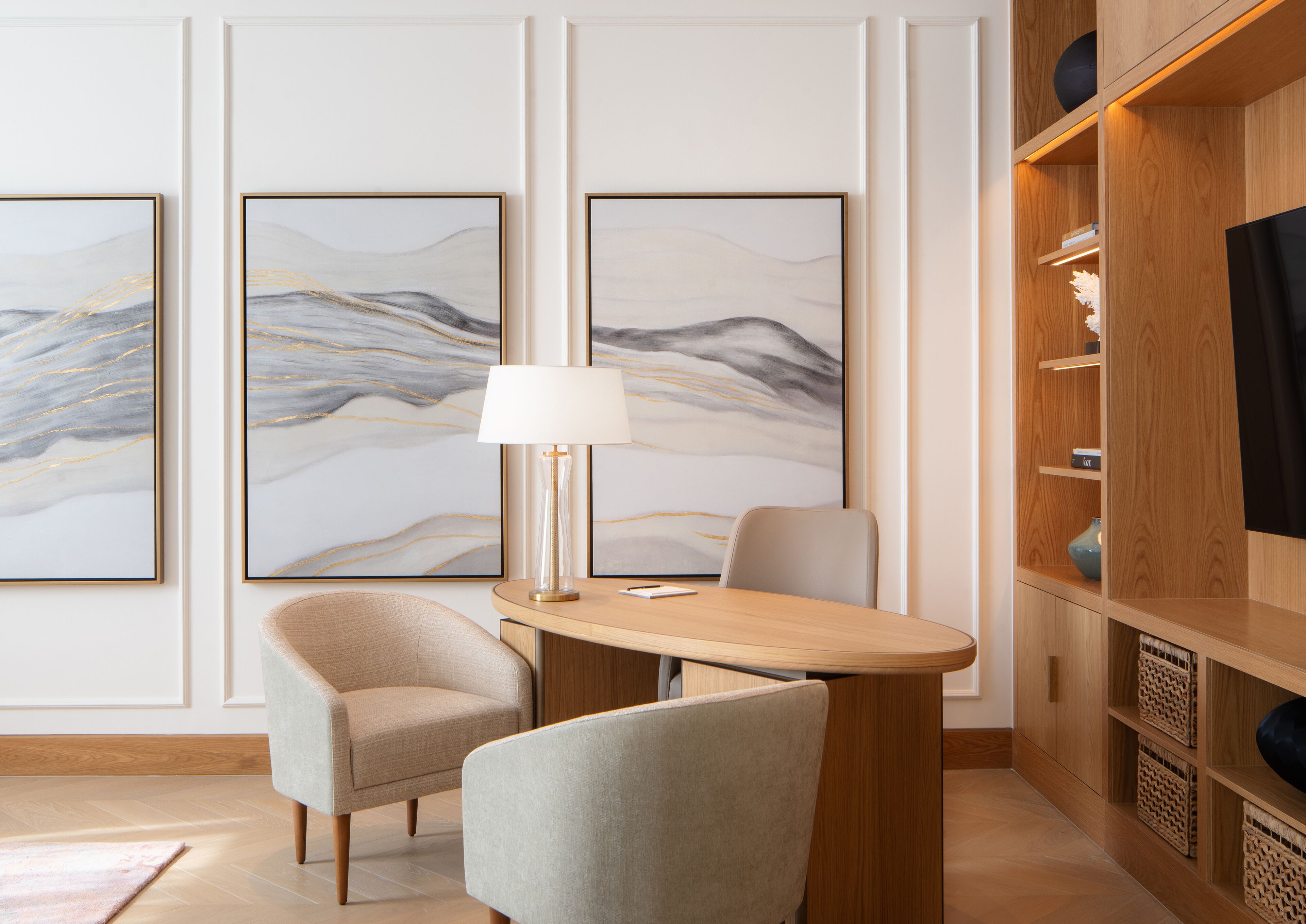 A modern room with a wooden table, two chairs, a lamp, and three large abstract paintings on the wall.