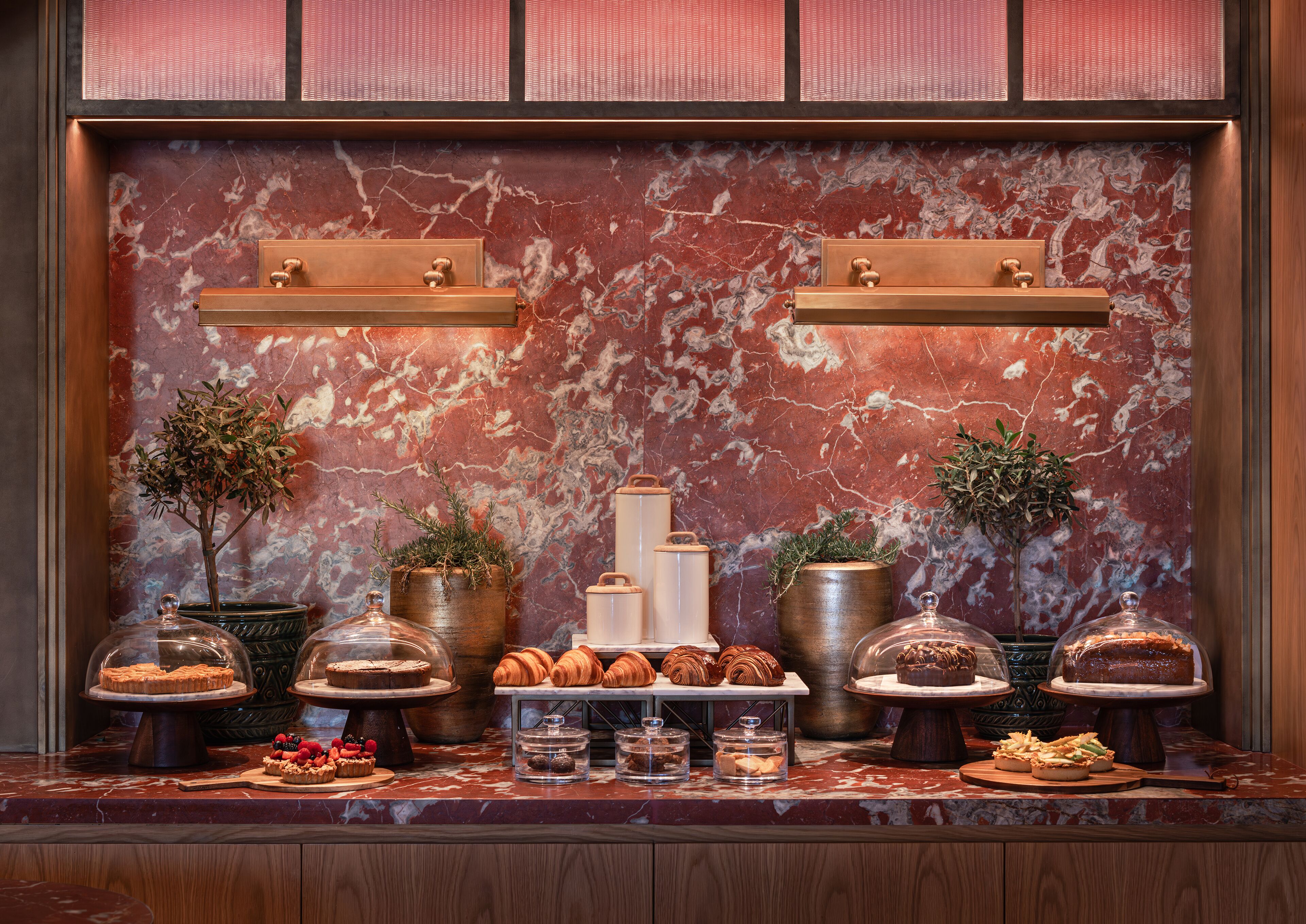 Una pared de mármol con una exhibición de pasteles y postres, incluyendo croissants y pasteles.
