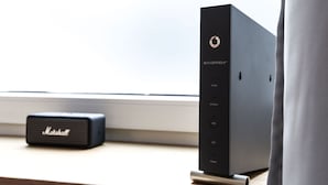 Ein schwarzer, Wi-Fi-zertifizierter 6-Router mit einem Marshall-Lautsprecher auf einer Holzoberfläche in der Nähe eines Fensters.