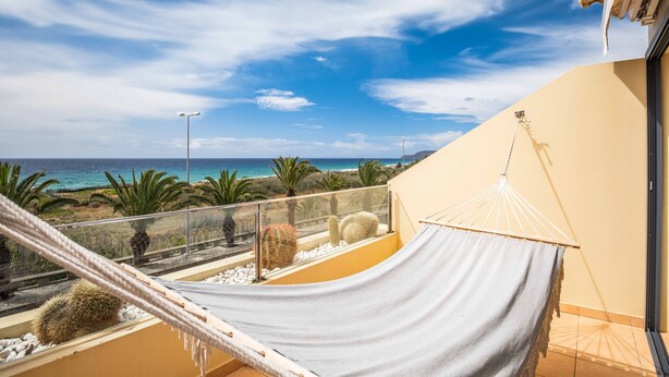 Un balcon avec un hamac, une vue sur la mer et un cactus.
