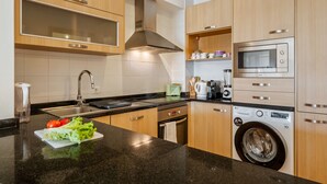 Une cuisine moderne avec des meubles en bois, un évier en acier inoxydable, un four encastré et un lave-linge à chargement frontal.