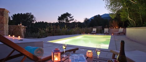 An outdoor pool area with lounge chairs, a table with drinks, and candles.