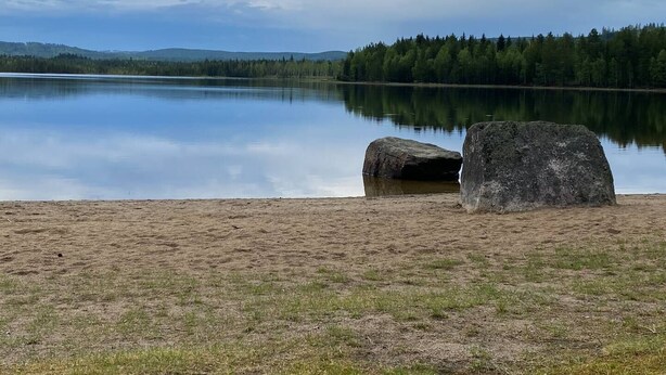 A calm lake with a sandy shore and two large rocks. - Ramsjö Camping (Ramsjö)