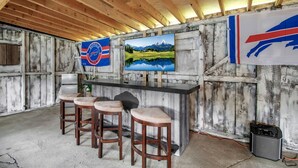 Un coin bar au style rustique, avec des poutres en bois, un comptoir en marbre et trois tabourets.
