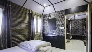 Une chambre à coucher moderne avec un lit, une fenêtre avec des rideaux, un mur orné d’un motif géométrique et une salle de bain visible à travers une porte ouverte.