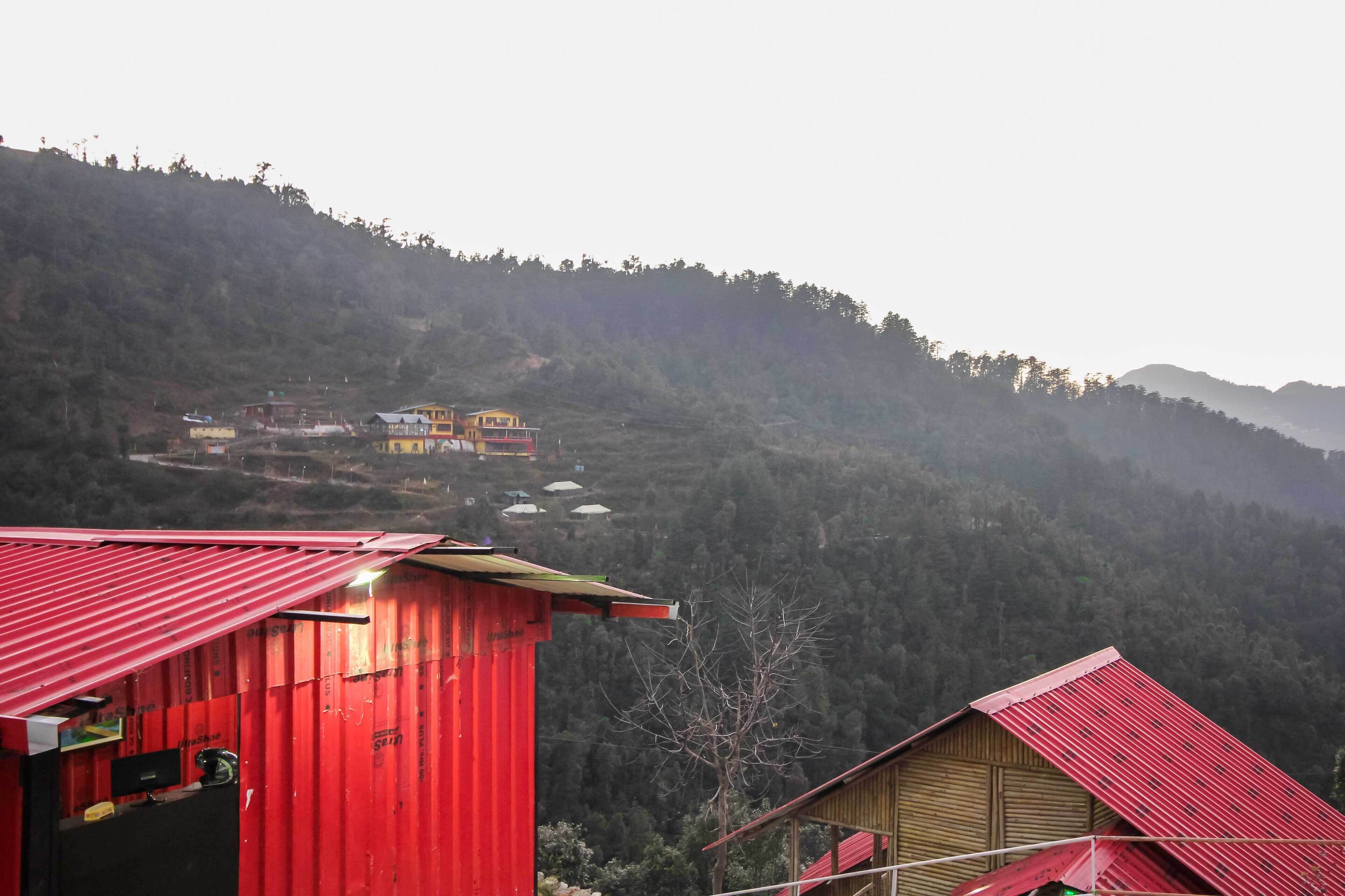 A red building with a corrugated metal roof, surrounded by a mountainous landscape.