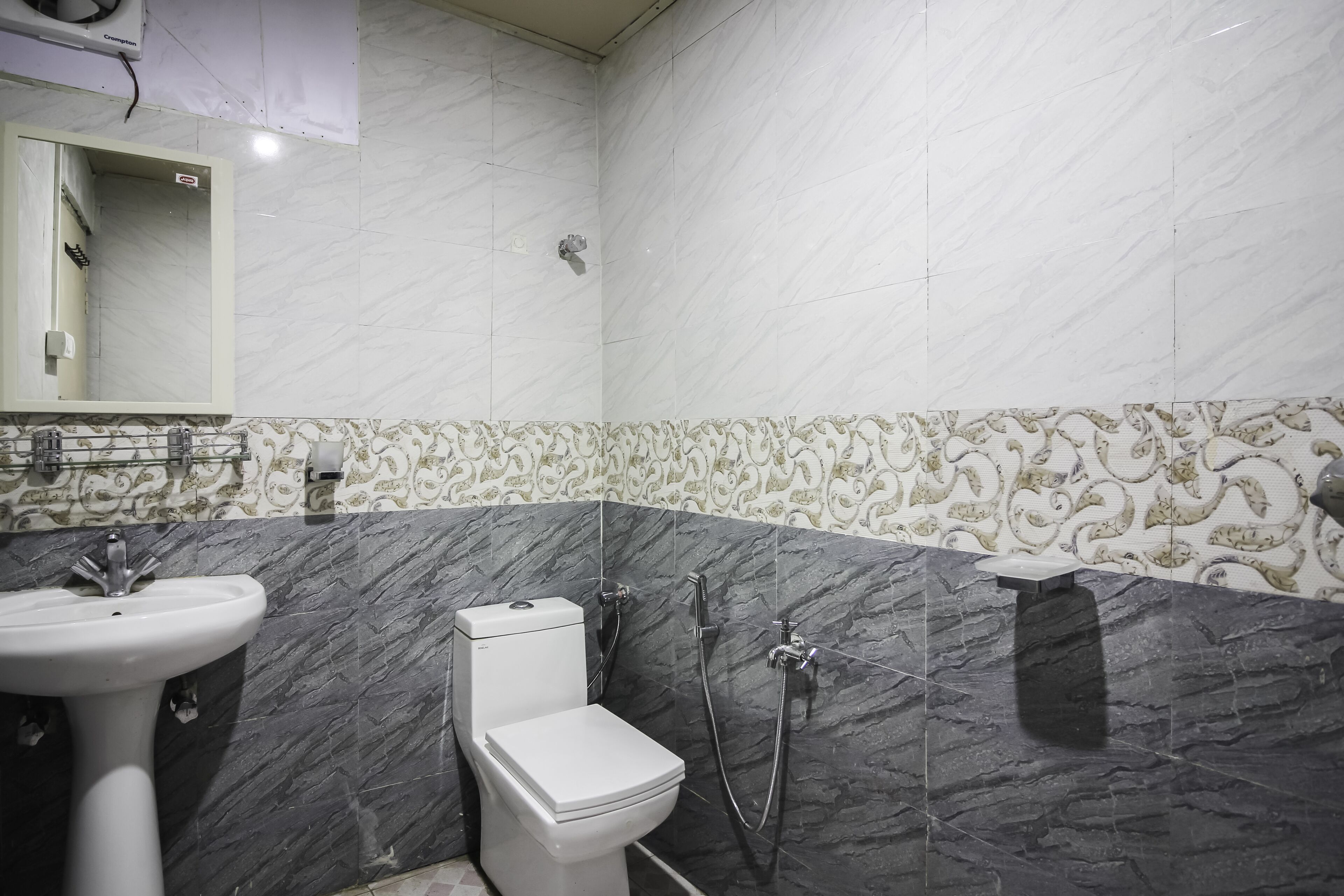 Un baño con lavamanos, inodoro y ducha blancos. Las paredes están revestidas con un diseño de mármol.