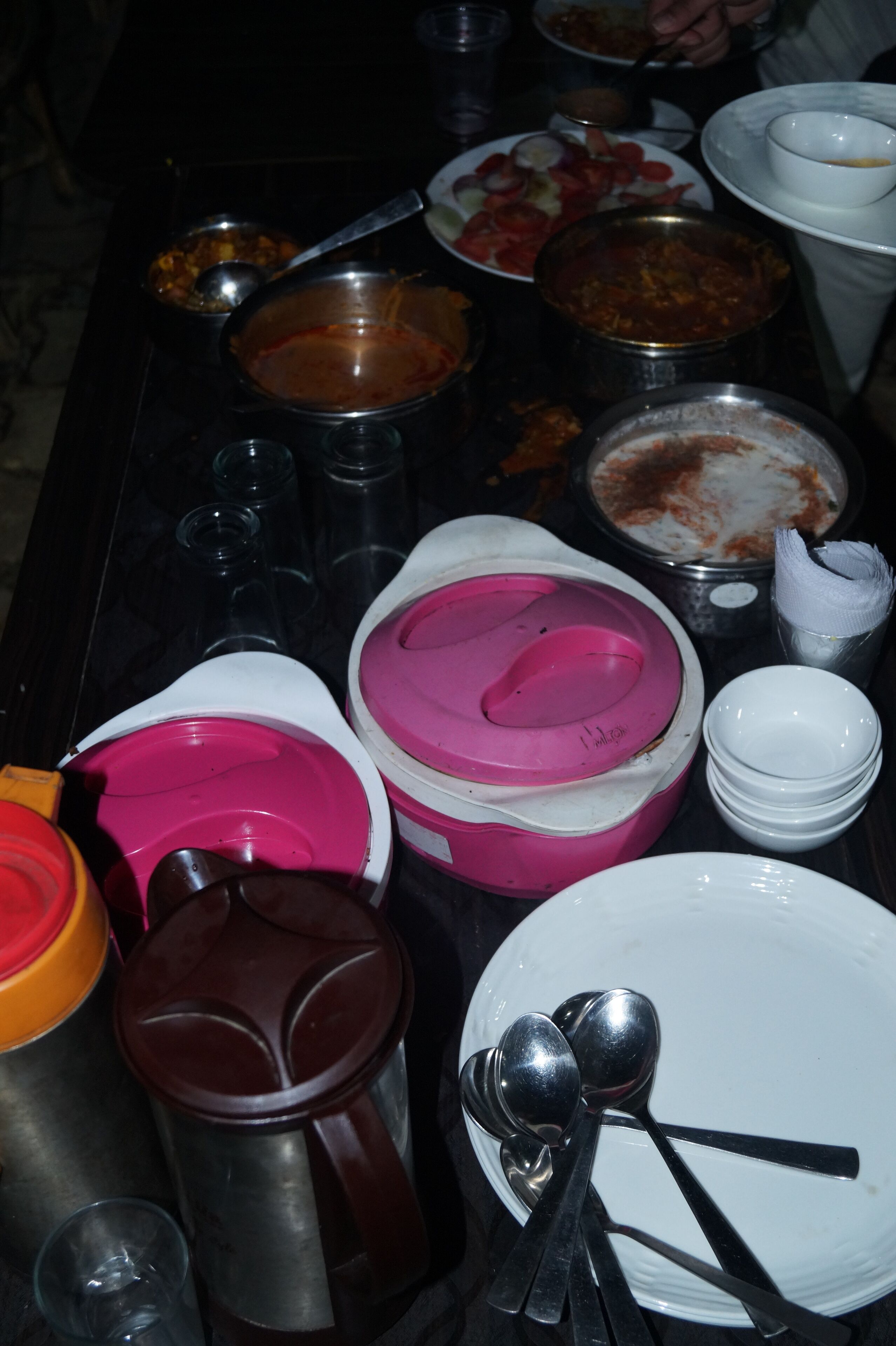A table with various dishes and utensils, including bowls, spoons, and a thermos.
