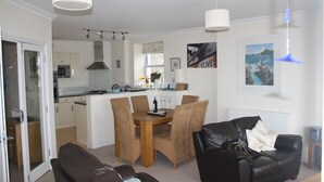 Una sala de estar moderna con un sofá de cuero marrón, una mesa de comedor con sillas y una cocina al fondo.
