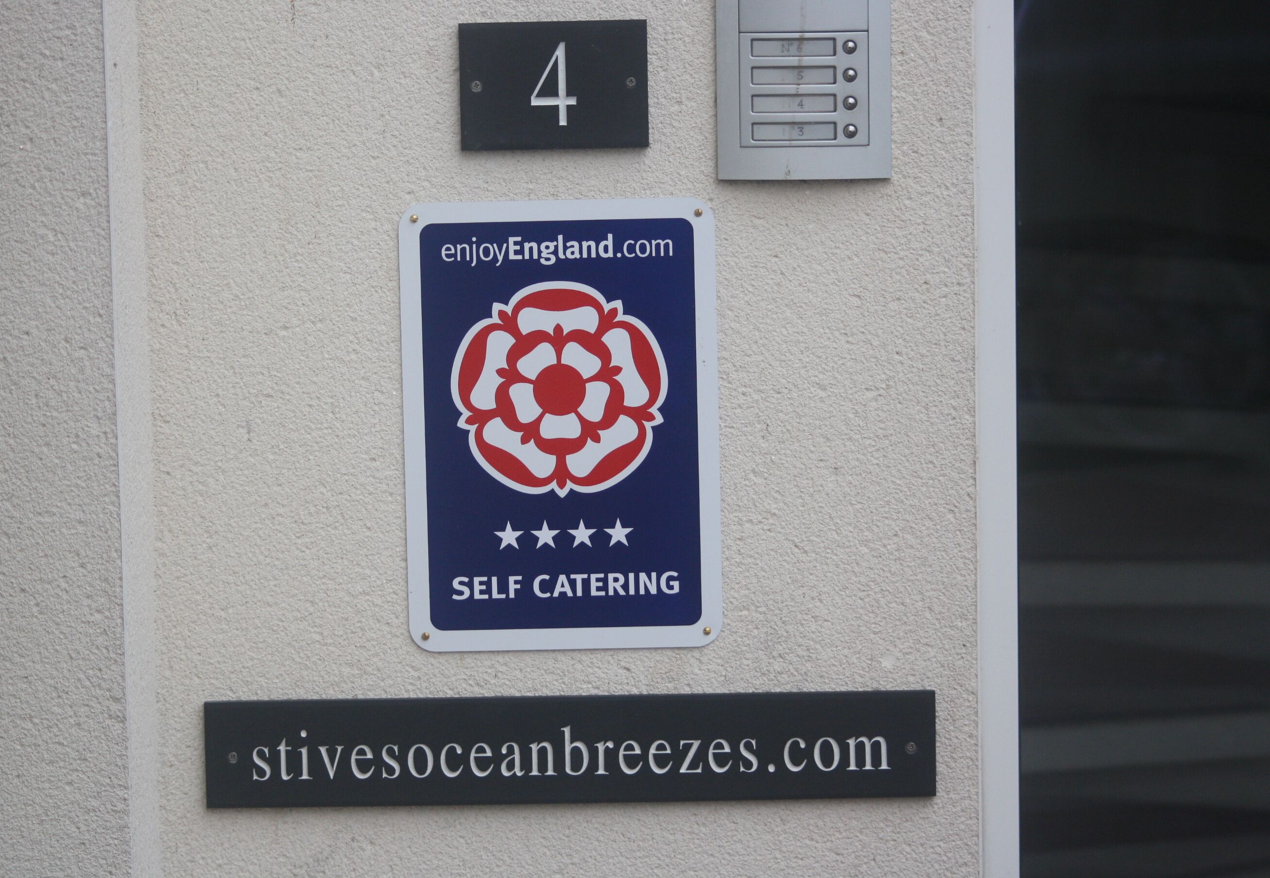Une enseigne indiquant un hébergement en location avec cuisine, accompagnée d’une adresse de site web et d’un logo représentant une fleur.