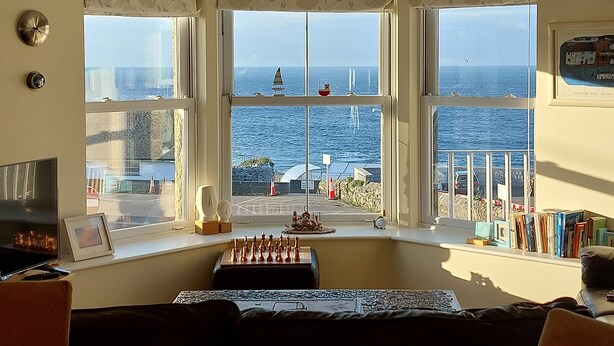 Una habitación con ventanal panorámico que da al mar, un tablero de ajedrez y una estantería.