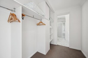 A walk-in closet with wooden hangers, a white ceiling, and a glass shower door. - “The Cove” 
Beachfront Retreat.
Wake to the Ocean. Unwind in Nature. (Korora)