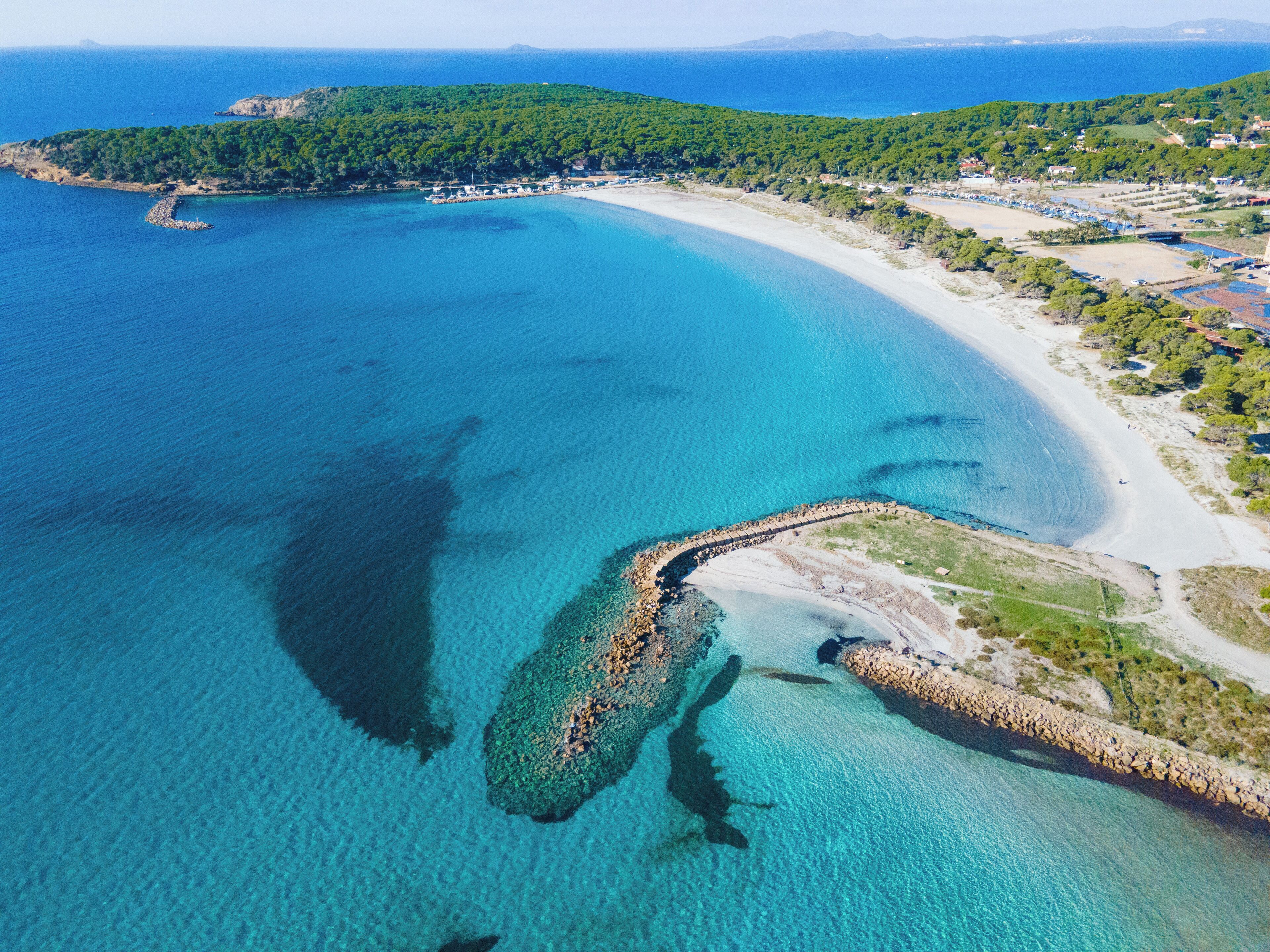 Vista aérea de una zona costera con aguas turquesas cristalinas, una playa de arena y un litoral rocoso.