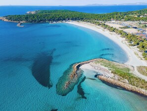 Vue aérienne d’une zone côtière avec des eaux turquoise limpides, une plage de sable et une côte rocheuse.