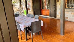 Un espace extérieur aménagé pour les repas, avec une table et des chaises, une terrasse couverte et une porte en bois.