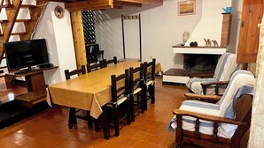 Un espace repas comprenant une longue table en bois, des chaises, un téléviseur, une cheminée et un escalier.