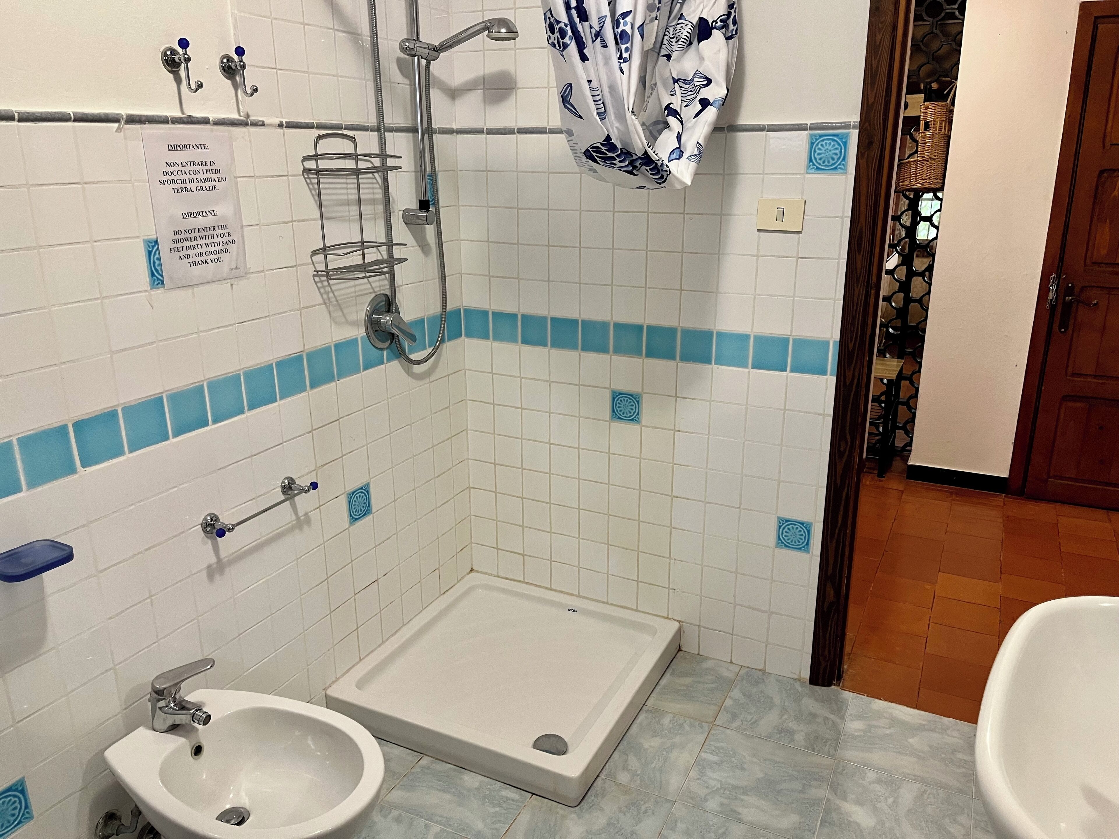 Un baño con ducha, lavabo e inodoro. Hay un cartel en la pared, un perchero y una cortina de ducha.