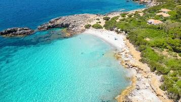 A coastal property with a beach, rocky shoreline, and greenery.