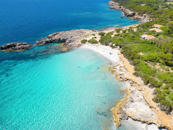 A coastal property with a beach, rocky shoreline, and greenery.