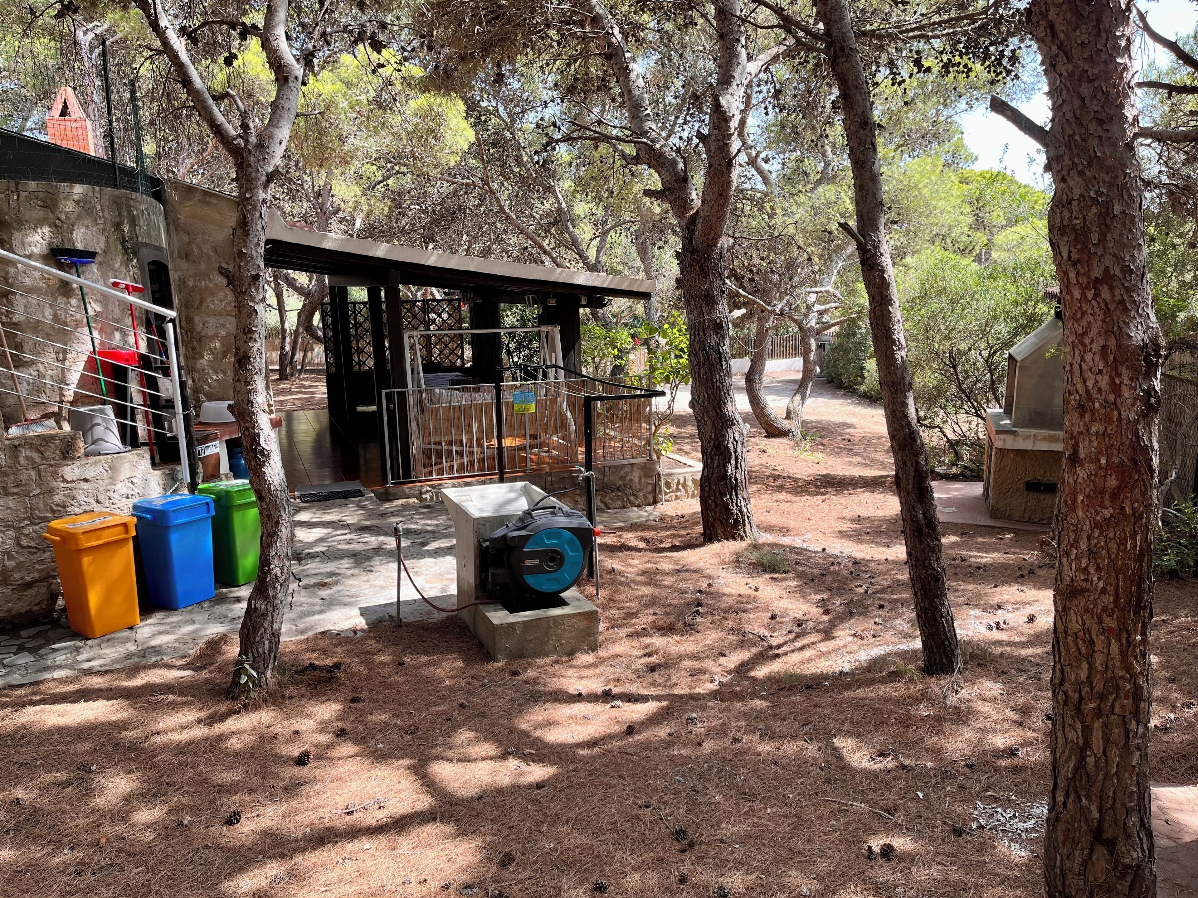 Un espacio al aire libre rústico con una estructura cubierta, una bomba de agua y recipientes de almacenamiento.