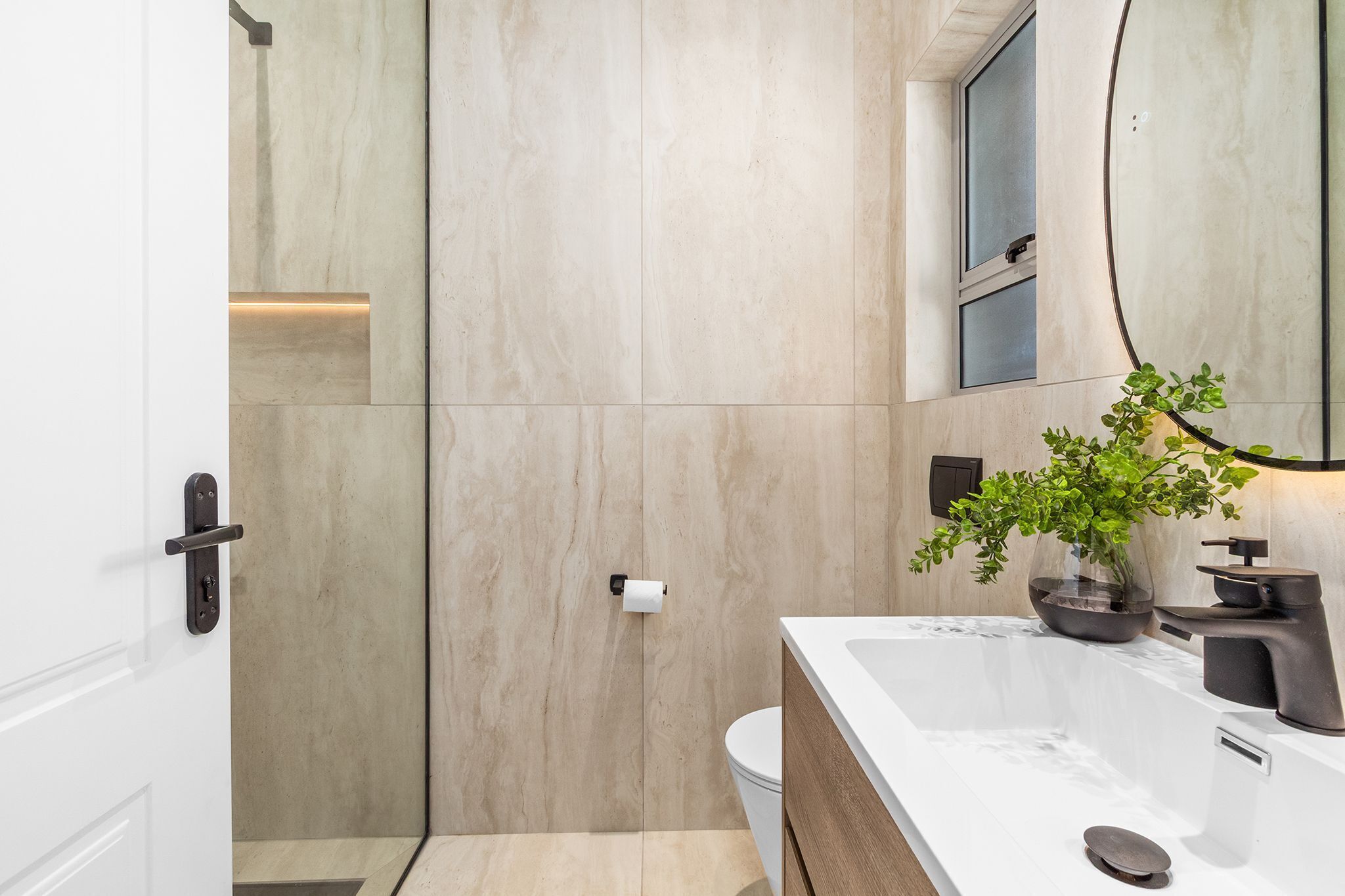 A modern bathroom with a large mirror, a sink with a dark faucet, and a toilet.