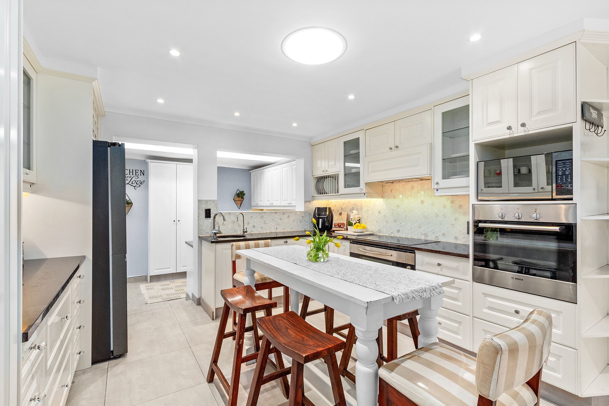 A modern kitchen with white cabinetry, a central island with stools, and a Bosch oven.