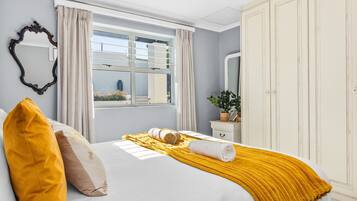 Une chambre à coucher bien rangée, avec un lit, une fenêtre avec des rideaux, une armoire et un miroir au mur.