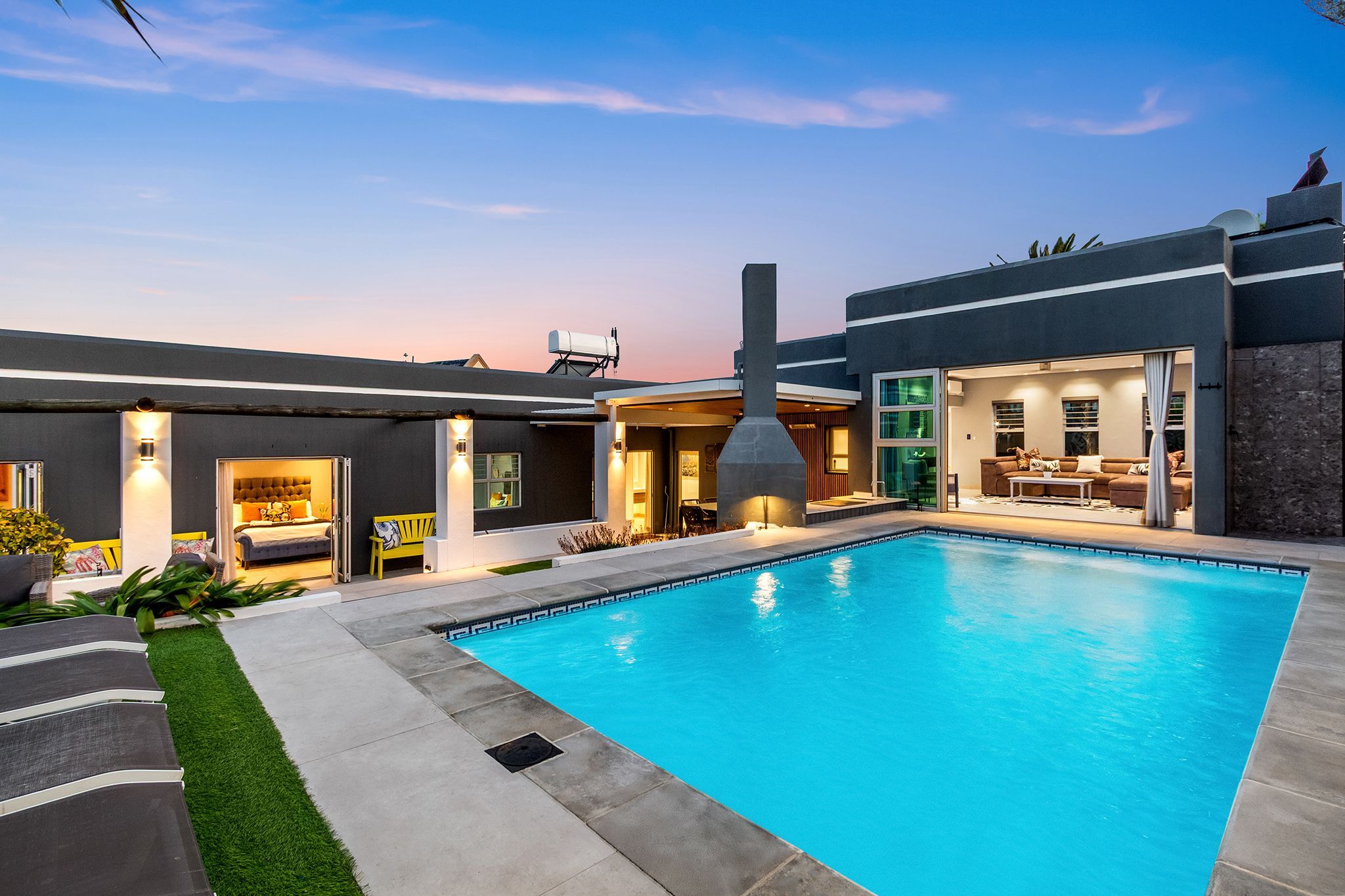A modern house with a swimming pool, a patio, and a well-lit interior.