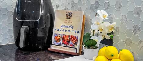 Un plan de travail de cuisine avec une machine à café, un livre de recettes intitulé « Les plats préférés des familles sud-africaines », une orchidée en pot et un bol de citrons.