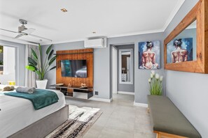 A modern bedroom with a bed, a TV mounted on a wooden panel, a ceiling fan, and a large window. - Rancho Relaxo (Cape Town)
