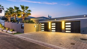 A modern building with a paved driveway, a garage with illuminated panels, and palm trees. - Rancho Relaxo (Cape Town)