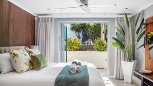 A modern bedroom with a bed, a ceiling fan, and a view of a balcony with plants. - Rancho Relaxo (Cape Town)