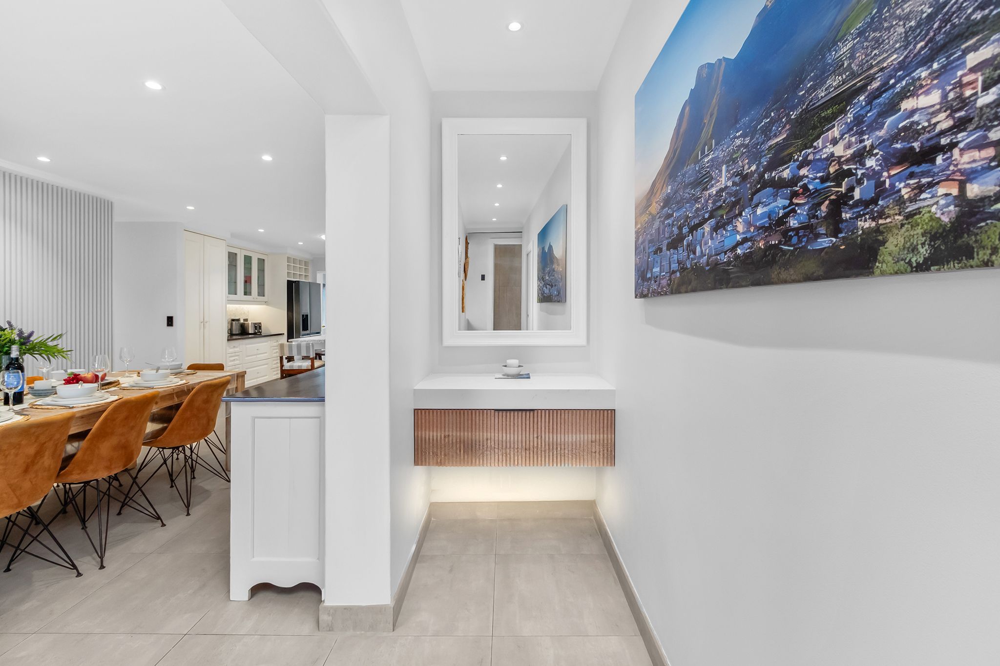 A modern kitchen with white cabinets, a built-in island, and a large cityscape painting on the wall.